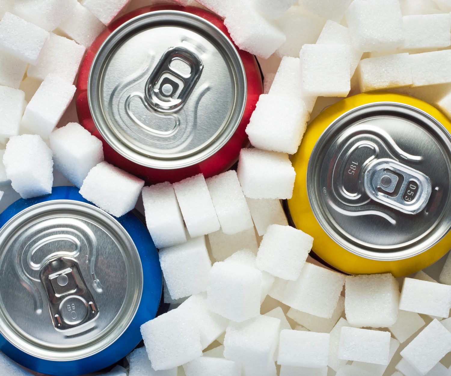 Unhealthy food concept - sugar in carbonated drinks. Sugar cubes as background and canned drinks