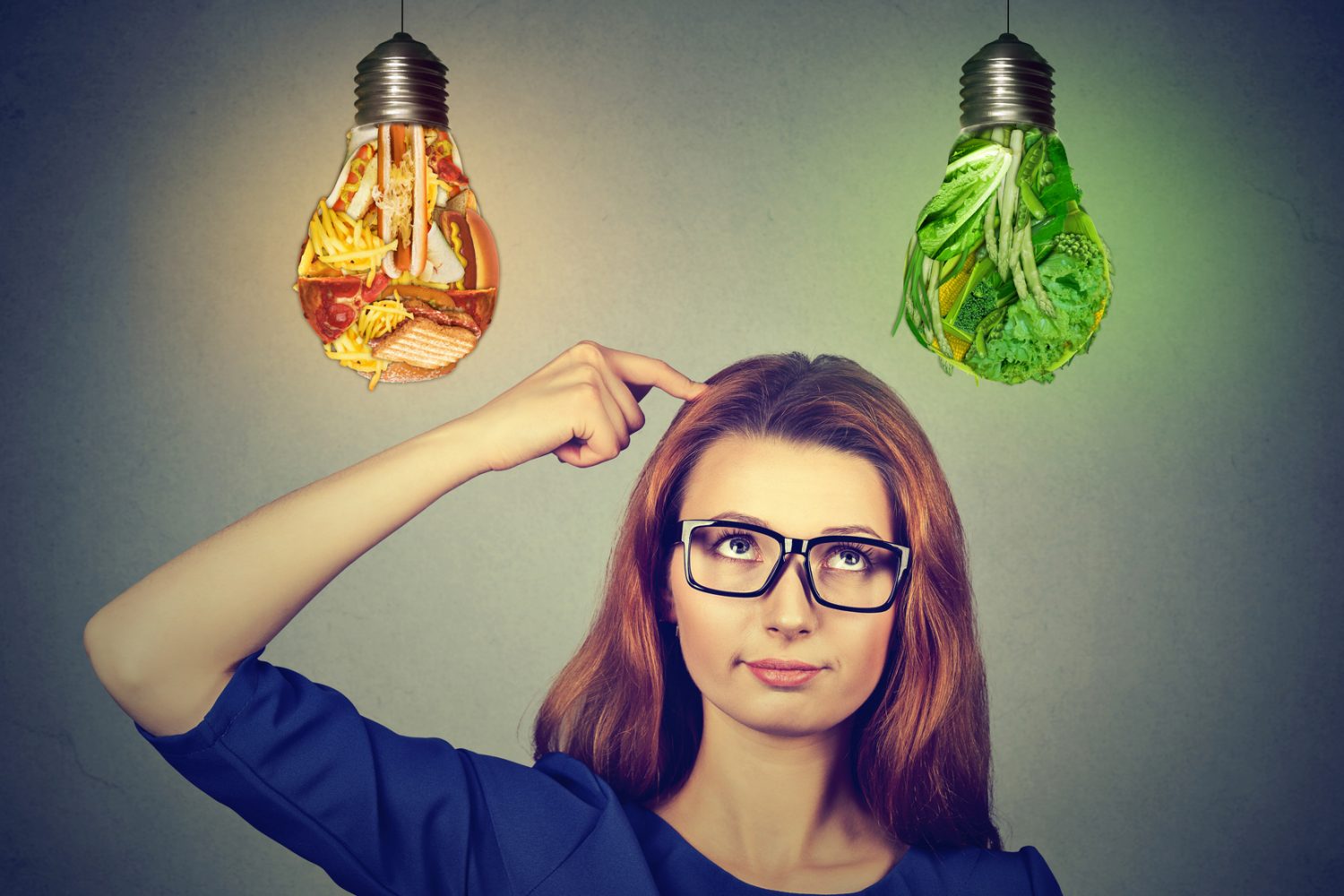 Woman in glasses thinking looking up at junk food and green vegetables light bulbs isolated on gray wall background. Diet choice right nutrition healthy lifestyle concept